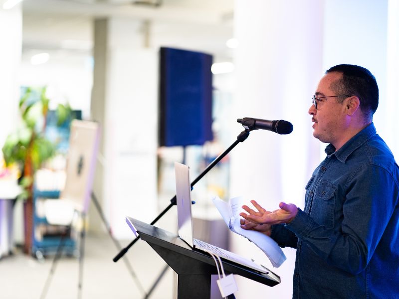 Chris E. Vargas stands in front of an audience seated in The Catalyst while presenting his slideshow on queer and transgender culture. 